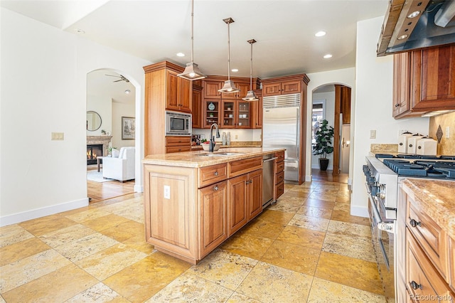 kitchen with arched walkways, a sink, wall chimney range hood, and built in appliances