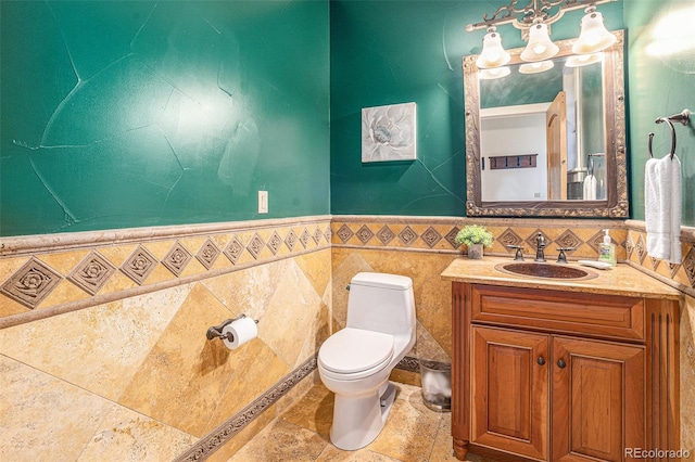 half bath featuring stone tile floors, toilet, a wainscoted wall, vanity, and tile walls