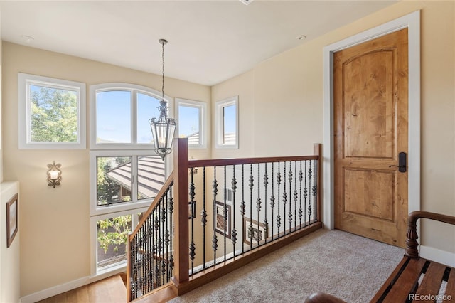 hallway featuring baseboards, carpet, an upstairs landing, and a notable chandelier