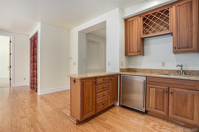 kitchen featuring a sink, baseboards, light wood-style floors, fridge, and brown cabinetry