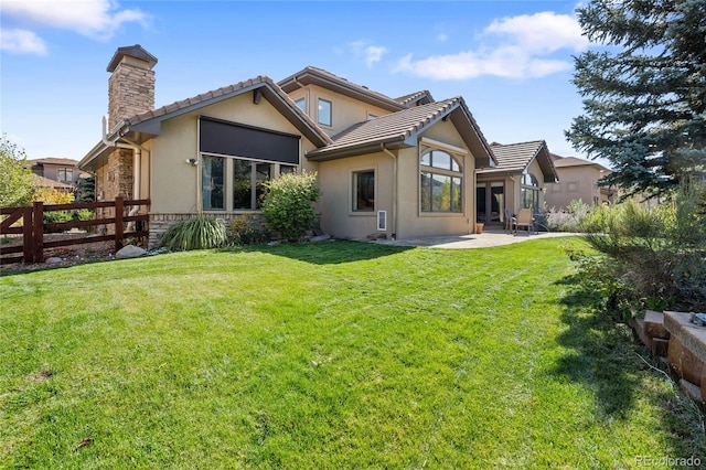 back of house featuring a lawn, a patio, a chimney, fence, and stucco siding