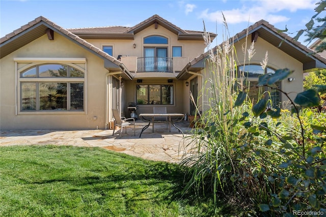 rear view of property with a patio area, a lawn, a balcony, and stucco siding