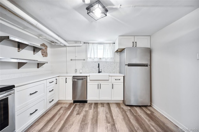 kitchen with sink, appliances with stainless steel finishes, white cabinets, light hardwood / wood-style floors, and backsplash