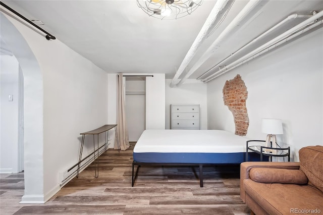 bedroom featuring hardwood / wood-style flooring, baseboard heating, and a closet