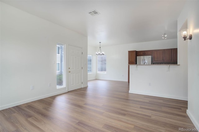 unfurnished living room with a notable chandelier and light hardwood / wood-style floors