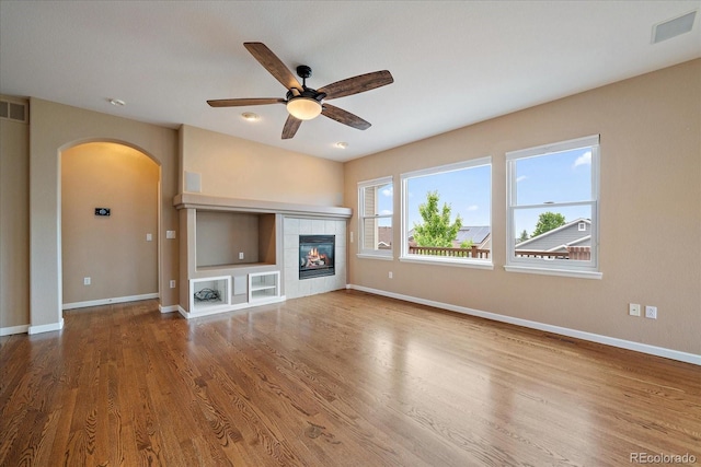 22873 E David Pl, Aurora, CO 80016 - unfurnished living room with arched walkways, a tiled fireplace, wood finished floors, and a ceiling fan