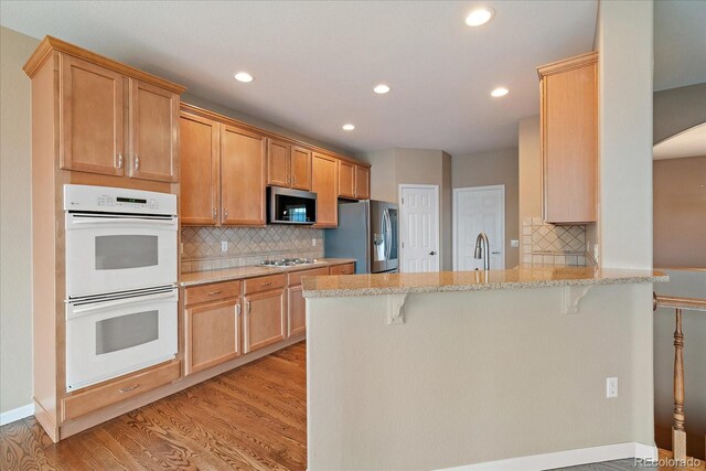 22873 E David Pl, Aurora, CO 80016 - kitchen featuring stainless steel appliances, a peninsula, recessed lighting, a breakfast bar area, and light wood-type flooring