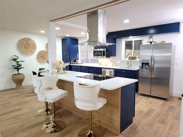 kitchen featuring a kitchen bar, island range hood, blue cabinets, sink, and appliances with stainless steel finishes