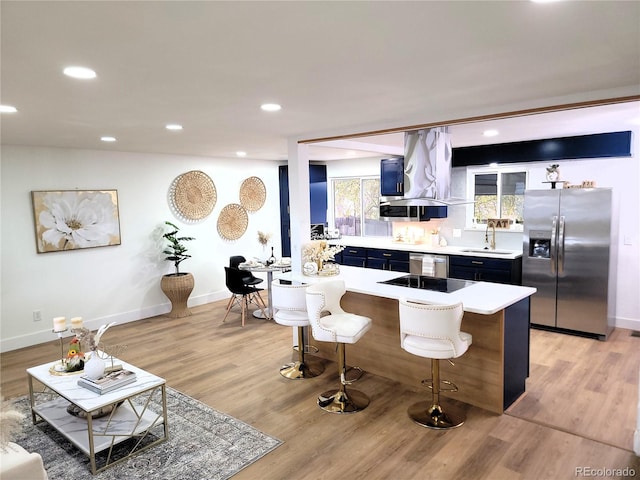 kitchen featuring island range hood, stainless steel appliances, a kitchen bar, sink, and light hardwood / wood-style floors