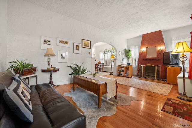 living room featuring hardwood / wood-style flooring, a textured ceiling, and a brick fireplace