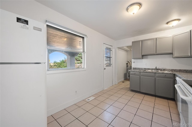 kitchen featuring gray cabinetry, sink, light tile patterned floors, and white appliances