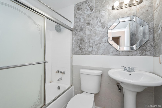 bathroom featuring tile walls, shower / bath combination with glass door, and toilet