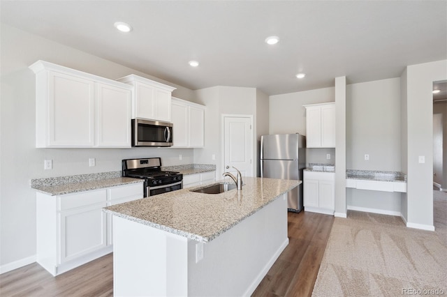 kitchen featuring sink, light stone counters, a kitchen island with sink, white cabinets, and appliances with stainless steel finishes