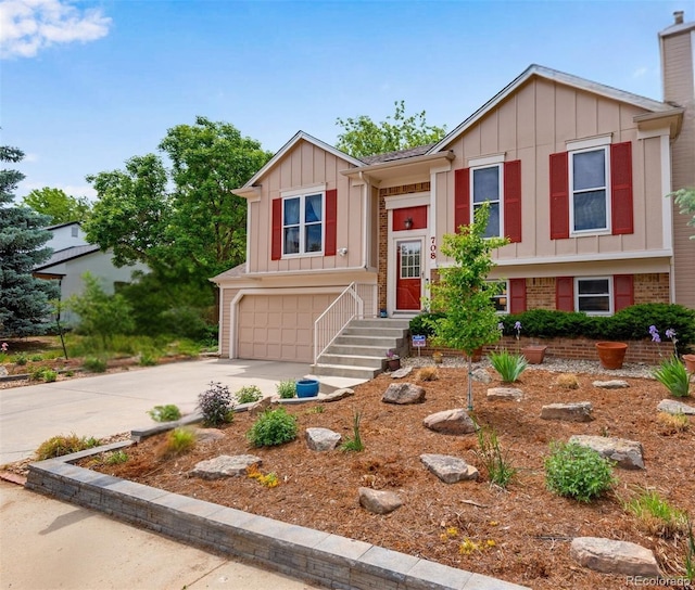 raised ranch with concrete driveway, a chimney, an attached garage, board and batten siding, and brick siding