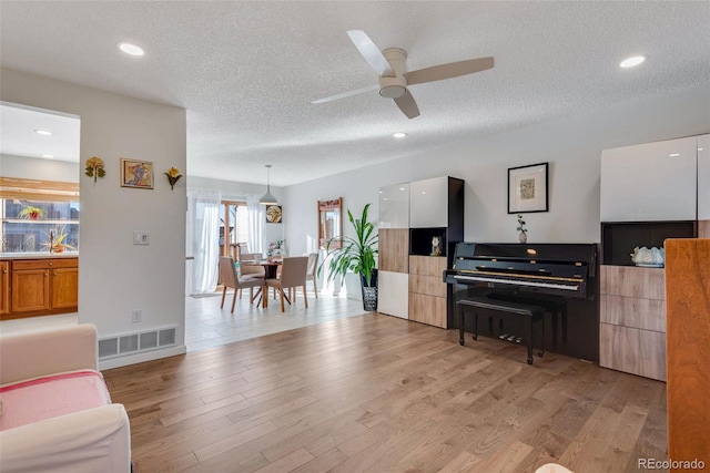 living area featuring recessed lighting, visible vents, light wood-style floors, a ceiling fan, and a textured ceiling