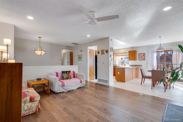 living room featuring visible vents, light wood-style flooring, and a textured ceiling