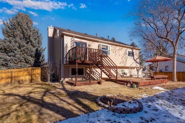 snow covered house with a deck, stairway, a chimney, and fence