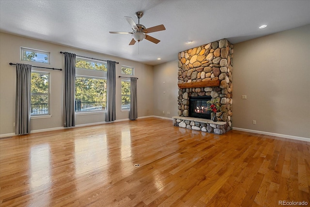 unfurnished living room with ceiling fan, a stone fireplace, light hardwood / wood-style floors, and a textured ceiling