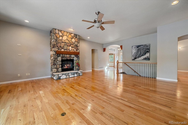 unfurnished living room featuring a stone fireplace, light hardwood / wood-style floors, ceiling fan, and a textured ceiling