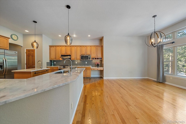 kitchen with sink, backsplash, hanging light fixtures, stainless steel appliances, and an island with sink