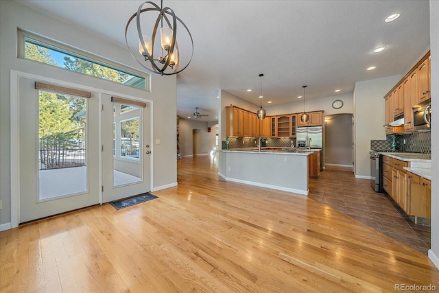 kitchen with tasteful backsplash, appliances with stainless steel finishes, light hardwood / wood-style flooring, and decorative light fixtures