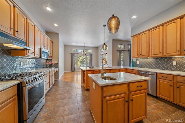 kitchen featuring a center island with sink, appliances with stainless steel finishes, pendant lighting, light stone countertops, and decorative backsplash