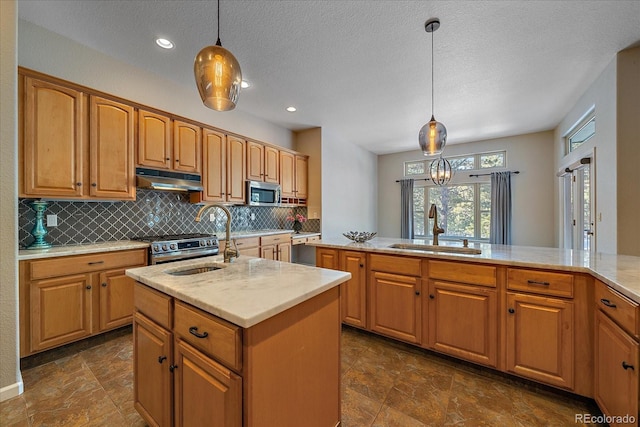 kitchen with appliances with stainless steel finishes, decorative light fixtures, sink, decorative backsplash, and a kitchen island with sink