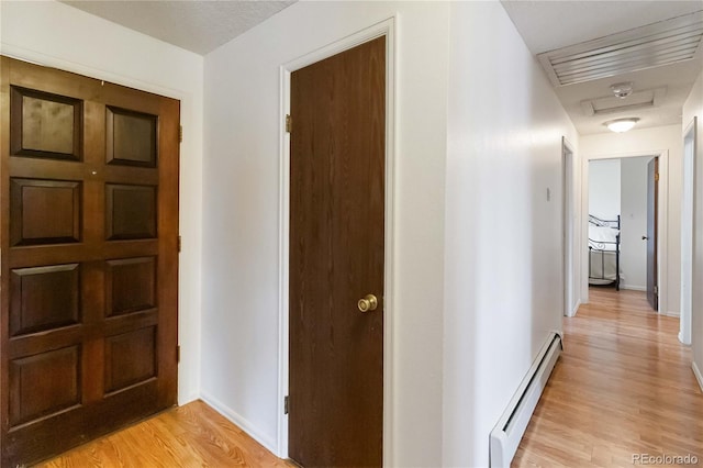 hallway with baseboard heating, light wood finished floors, and baseboards