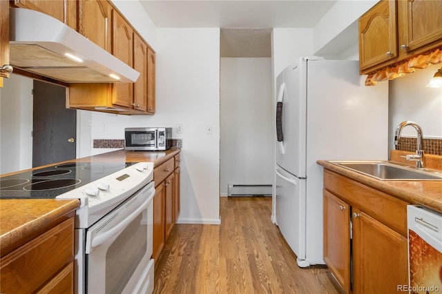 kitchen with white appliances, baseboard heating, a sink, under cabinet range hood, and brown cabinets