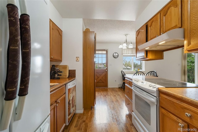 kitchen featuring white appliances, under cabinet range hood, a chandelier, and healthy amount of natural light