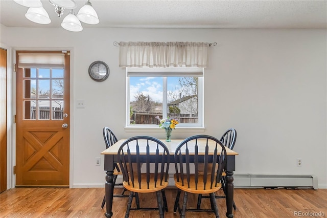 dining room featuring a chandelier, plenty of natural light, baseboard heating, and wood finished floors