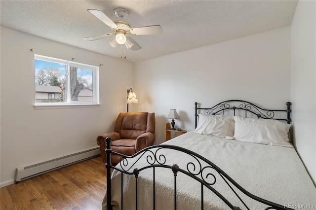 bedroom with a baseboard heating unit, wood finished floors, a textured ceiling, ceiling fan, and baseboards