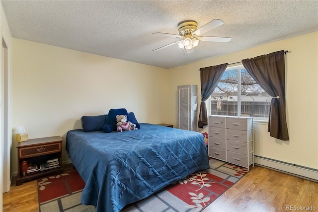 bedroom featuring light wood finished floors, baseboard heating, a textured ceiling, and ceiling fan