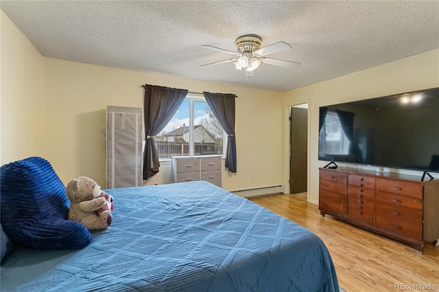 bedroom featuring a baseboard heating unit, light wood finished floors, a textured ceiling, and a ceiling fan