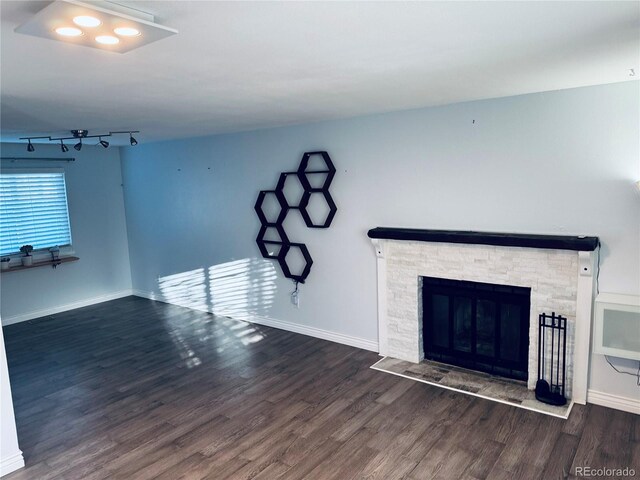 unfurnished living room with dark hardwood / wood-style floors, a stone fireplace, and rail lighting