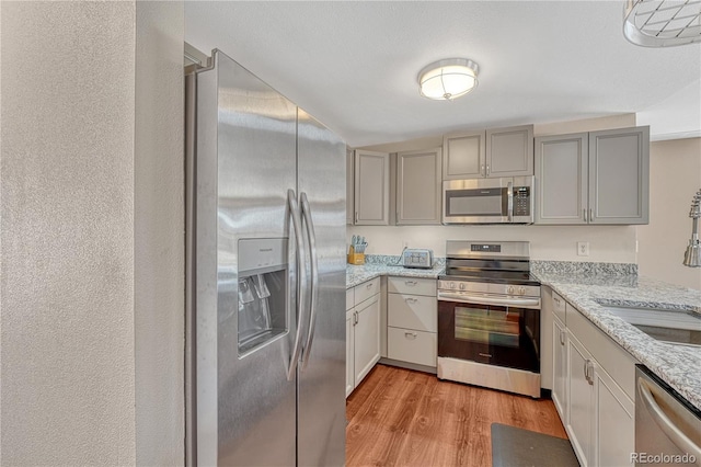 1786 Wintergreen Pl, Loveland, CO 80537 - kitchen featuring light wood-style flooring, light stone countertops, stainless steel appliances, gray cabinetry, and a sink