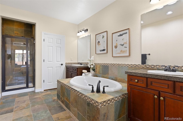 bathroom featuring a stall shower, a garden tub, two vanities, and stone finish flooring