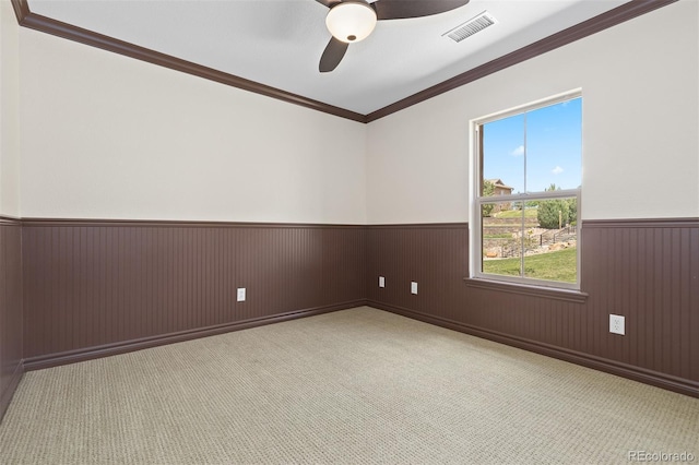 carpeted spare room featuring a wainscoted wall, ceiling fan, and crown molding