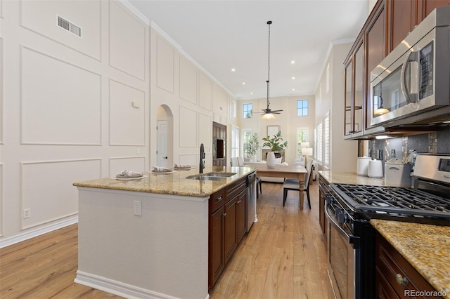 kitchen featuring appliances with stainless steel finishes, a sink, light wood-type flooring, open floor plan, and a ceiling fan