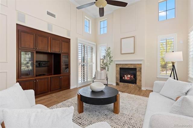 living area featuring light wood-type flooring, crown molding, a high ceiling, ceiling fan, and a tile fireplace