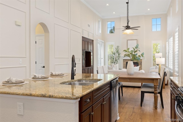 kitchen featuring a sink, a ceiling fan, stainless steel dishwasher, a towering ceiling, and light wood-style flooring
