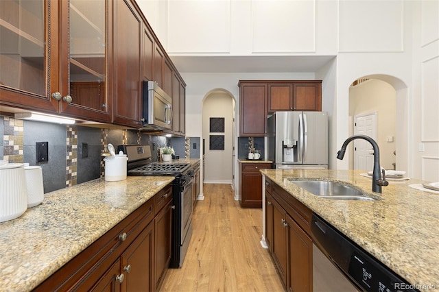 kitchen featuring stainless steel appliances, arched walkways, a sink, and light wood finished floors