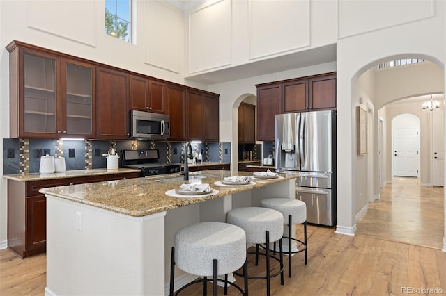 kitchen featuring arched walkways, appliances with stainless steel finishes, a high ceiling, a sink, and light wood finished floors