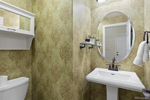 half bathroom featuring wallpapered walls, toilet, and a sink