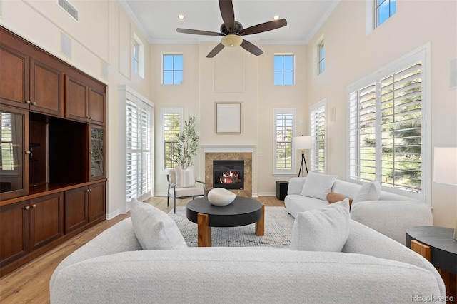 living room with ornamental molding, light wood-style floors, ceiling fan, a high end fireplace, and a towering ceiling