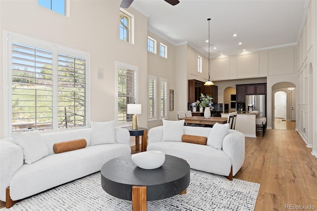 living area featuring arched walkways, a towering ceiling, ceiling fan, light wood-style flooring, and ornamental molding