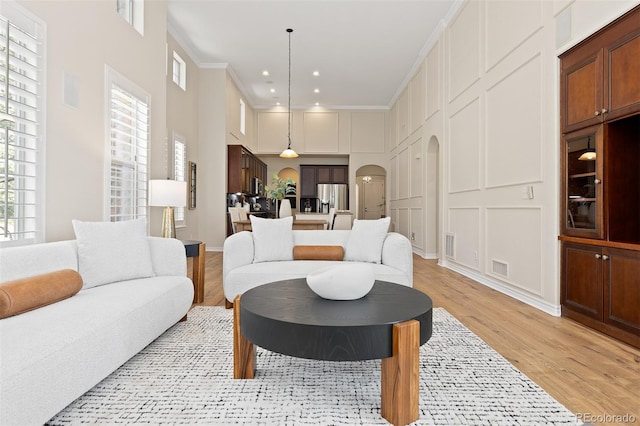 living area with arched walkways, light wood-type flooring, plenty of natural light, recessed lighting, and ornamental molding