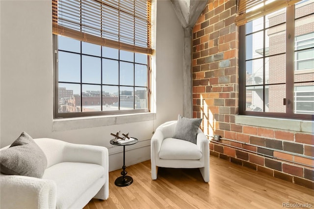 sitting room featuring brick wall, light wood-type flooring, and a wealth of natural light