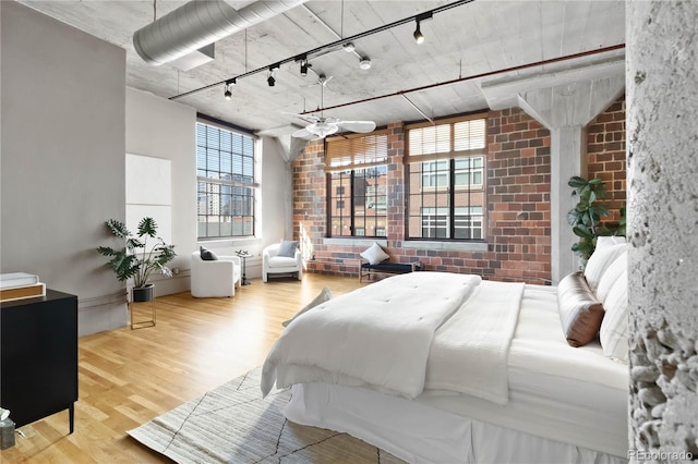 bedroom with brick wall, hardwood / wood-style floors, and track lighting