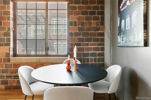 dining space featuring wood-type flooring and brick wall